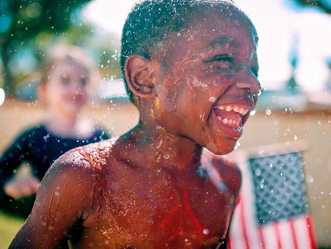 A smiling young black boy splashing in the water. 