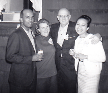 black and white photo of two men and two women with their arms around each other and smiling