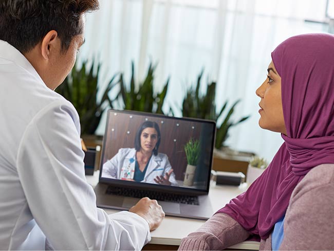 man and woman seated in front of computer screen with video call to physician