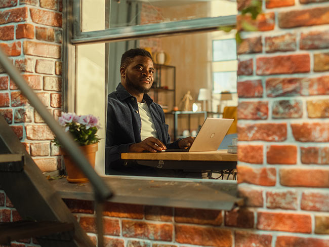 Man looking out the window while sitting in front of a laptop