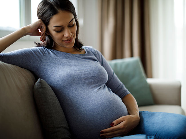 Smiling pregnant person holding belly on couch