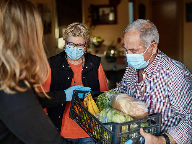 Elderly couple wearing face masks receiving a basket of groceries