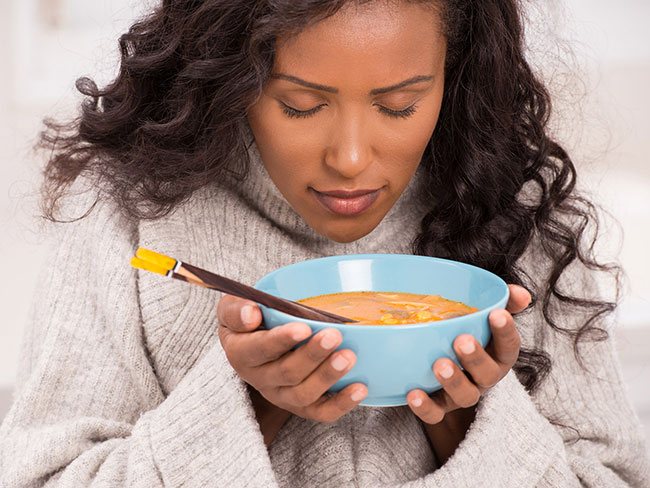woman looking downward at a bowl of soup that she is holding up close to her face