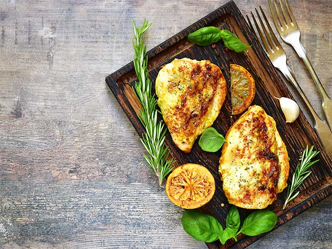 Lemon rosemary pork chops on a wooden cutting board with sprigs of rosemary and a grilled lemon on the side.