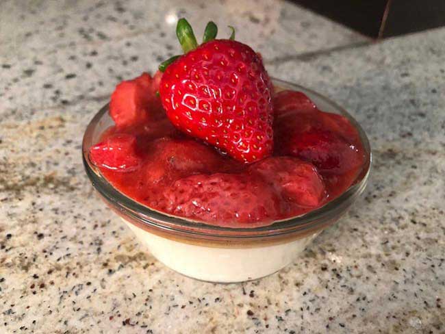 Baked parfait with strawberries on top in small, glass bowl.