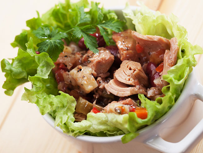 Bowl lined with lettuce leaves and filled with a mixture of tuna, diced red bell peppers and seasonings
