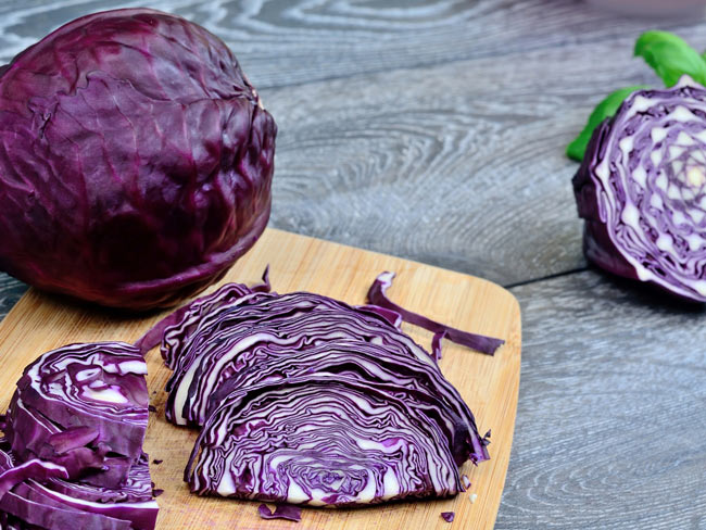 Red cabbage, both whole and cut, displayed on cutting board