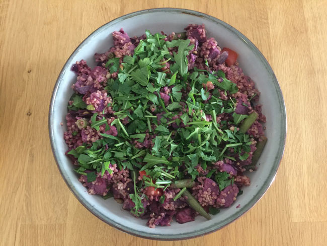 Overhead picture of purple potatoes, millet, and arugula in a bowl.